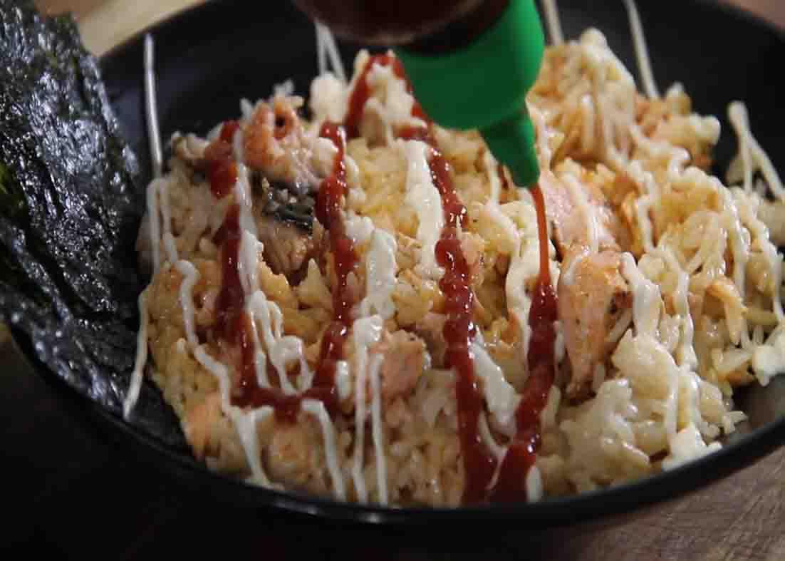 Drizzling the salmon rice bowl with some mayo and sriracha