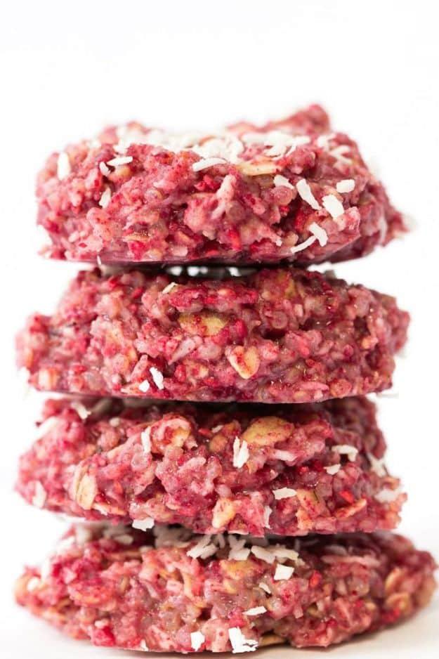 No bake raspberry quinoa cookies, four bright pink oat and coconut cookies stacked on a white surface