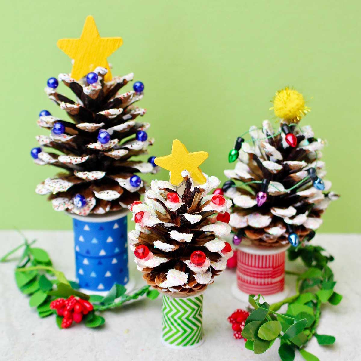 Three pinecone Christmas trees with white painted tips, glitter, bead lights and yellow wooden stars on washi tape spools