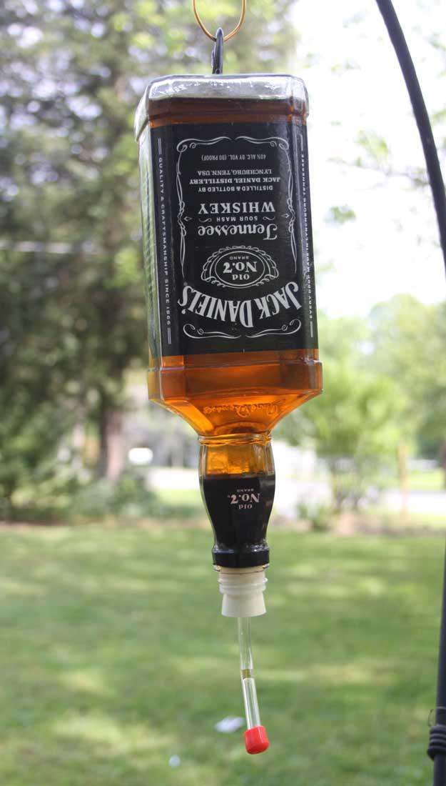 Hummingbird feeder made from a whiskey bottle hung upside down with a glass feeding tube in a garden