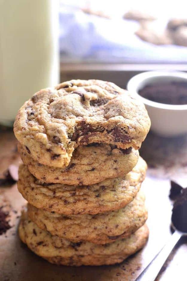 Stack of thick espresso chocolate chip cookies with one bite taken, a mug of coffee blurred behind them