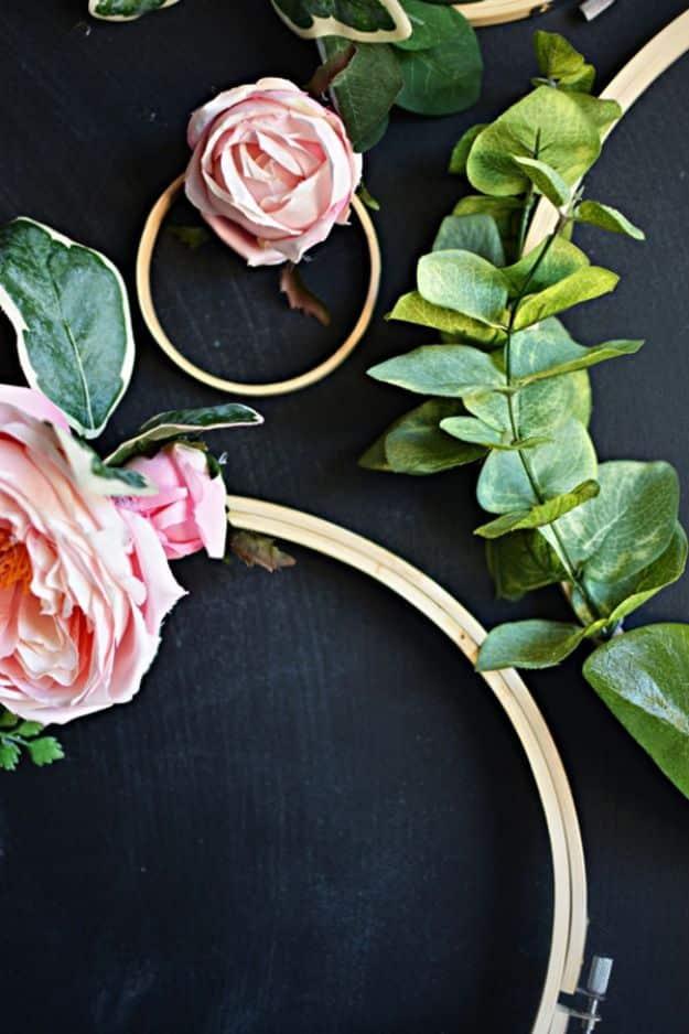 Gold embroidery hoops wrapped with pink faux roses and green eucalyptus leaves on a dark gray background