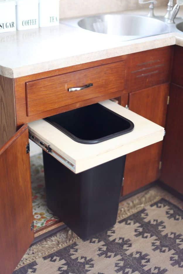 Oak kitchen base cabinet with the door open showing a tall black trash bin on a plywood pull out shelf