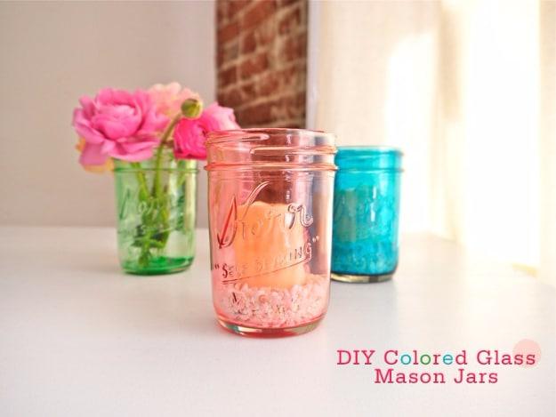 Three mason jars tinted pink, green and turquoise on a white sill, two holding pink roses against a brick wall