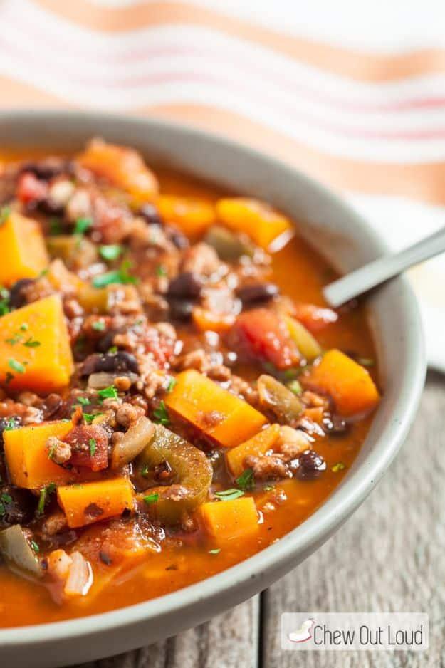 Butternut squash chili with orange squash cubes and black beans in a gray bowl with a striped napkin