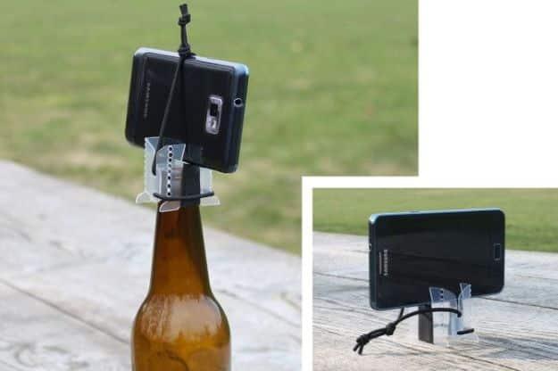 Smartphone tripod, a phone upright in a folded plastic bracket set into the neck of a brown bottle, with a table inset