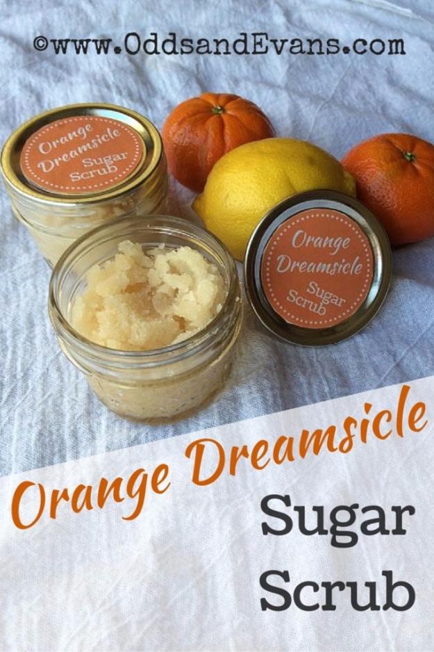 Orange dreamsicle sugar scrub in two small jars with orange labels, fresh oranges and a lemon behind