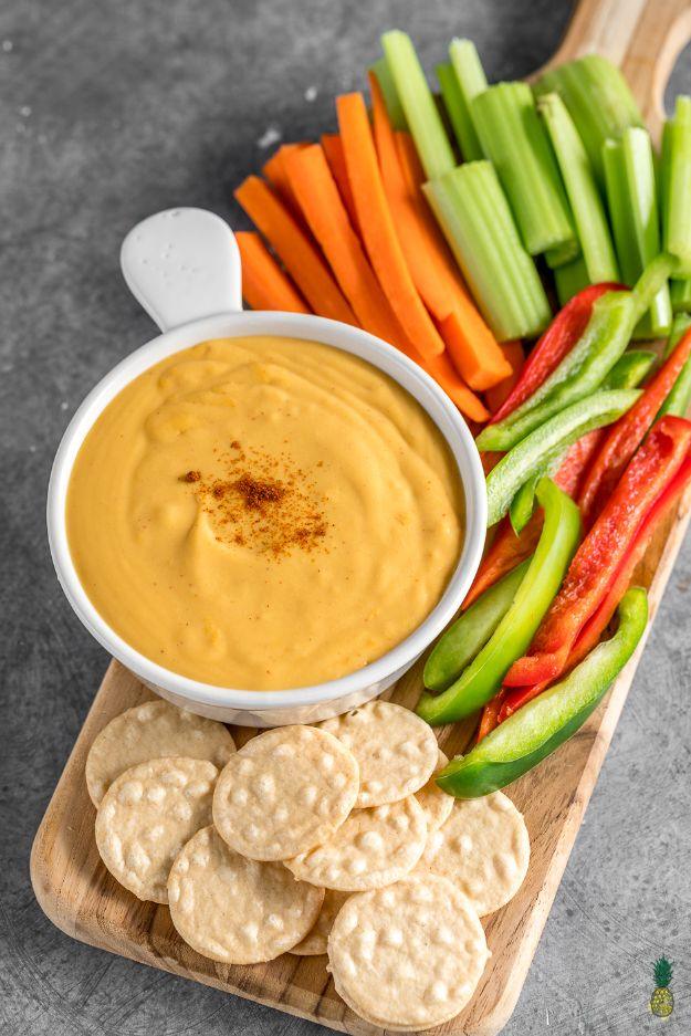 Vegan chipotle cheddar cheese sauce, a smooth orange dip in a bowl beside crackers and cut raw vegetables