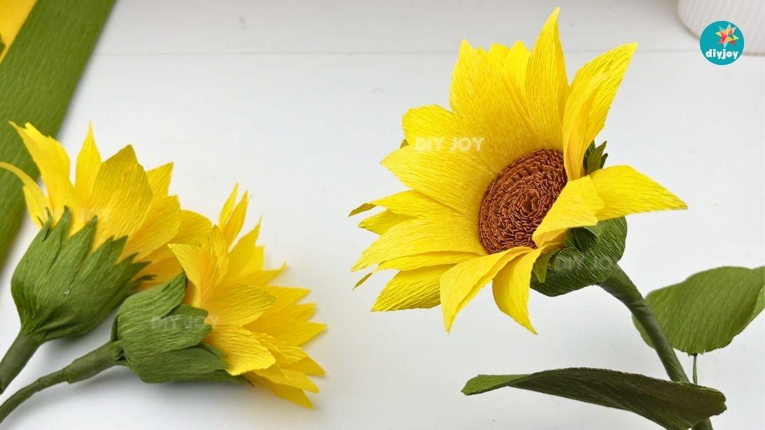 Crepe paper sunflower with a textured brown center and yellow petals beside green crepe paper leaves