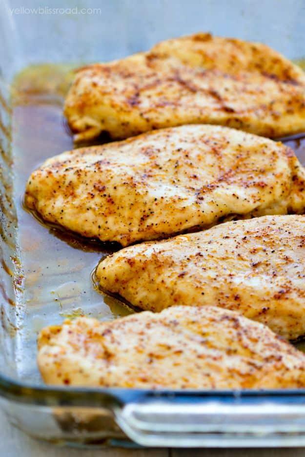 Baked chicken breasts in a glass baking dish, dusted golden with smoked paprika and resting in their own juices