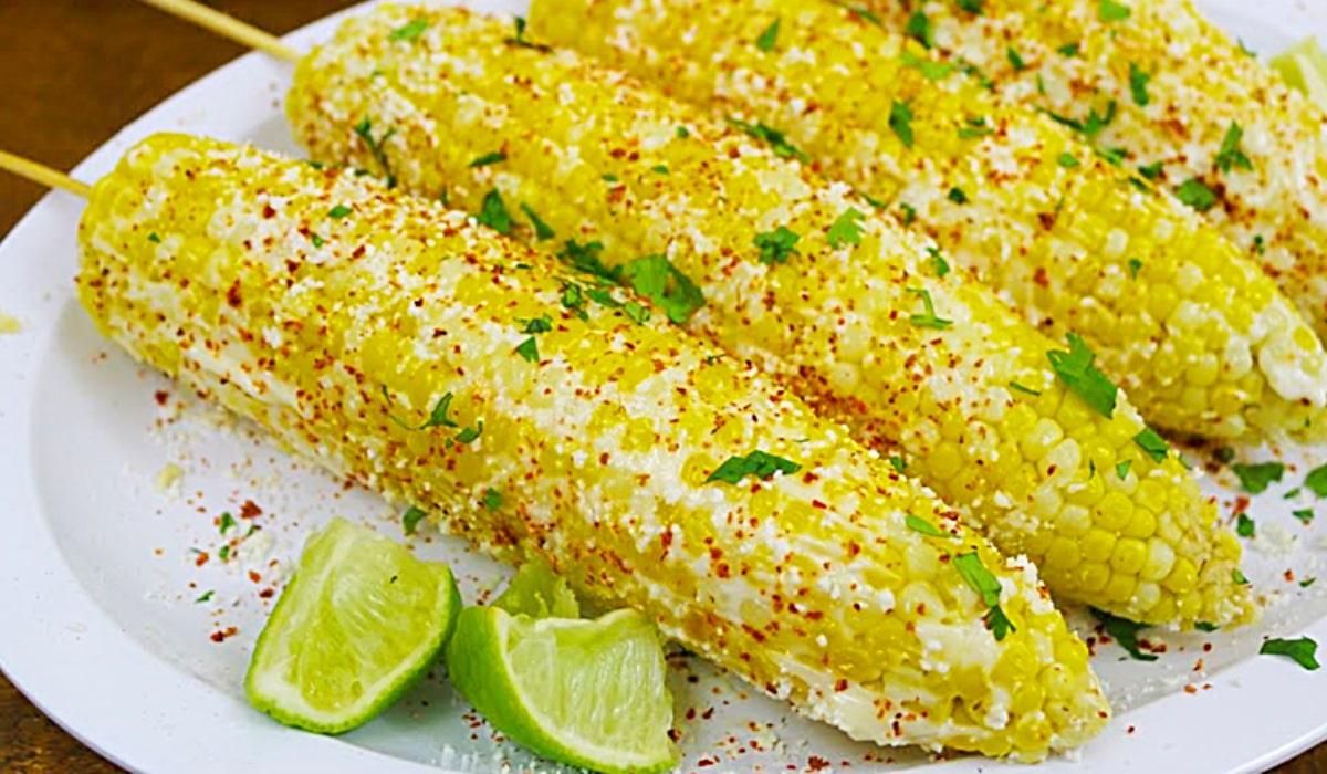 Mexican grilled street corn on the cob coated in mayo, parmesan, cilantro and chili powder on a cookout table