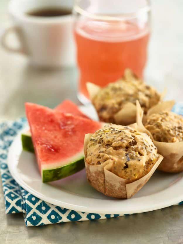 Watermelon chia seed muffins in brown paper liners on a plate beside two wedges of fresh cut watermelon