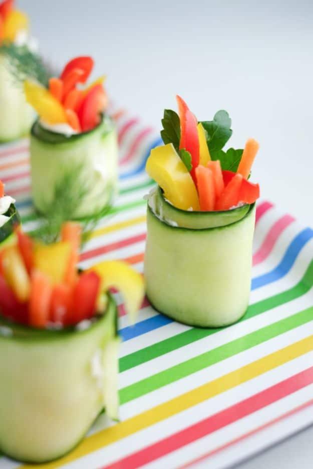 Cucumber ribbon roll ups standing upright filled with carrot and red and yellow pepper sticks on a striped cloth