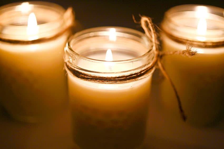 Three lit mason jar candles in cream soy wax on a dark surface, the middle jar tied with a strand of twine