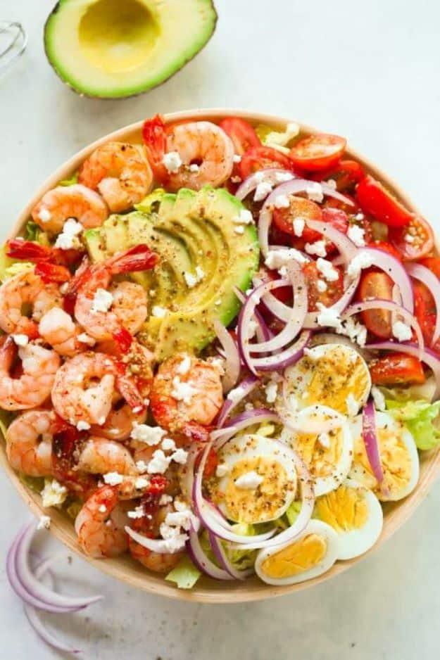 Shrimp avocado tomato salad in a bowl with seared shrimp, sliced avocado, boiled eggs, red onion and feta