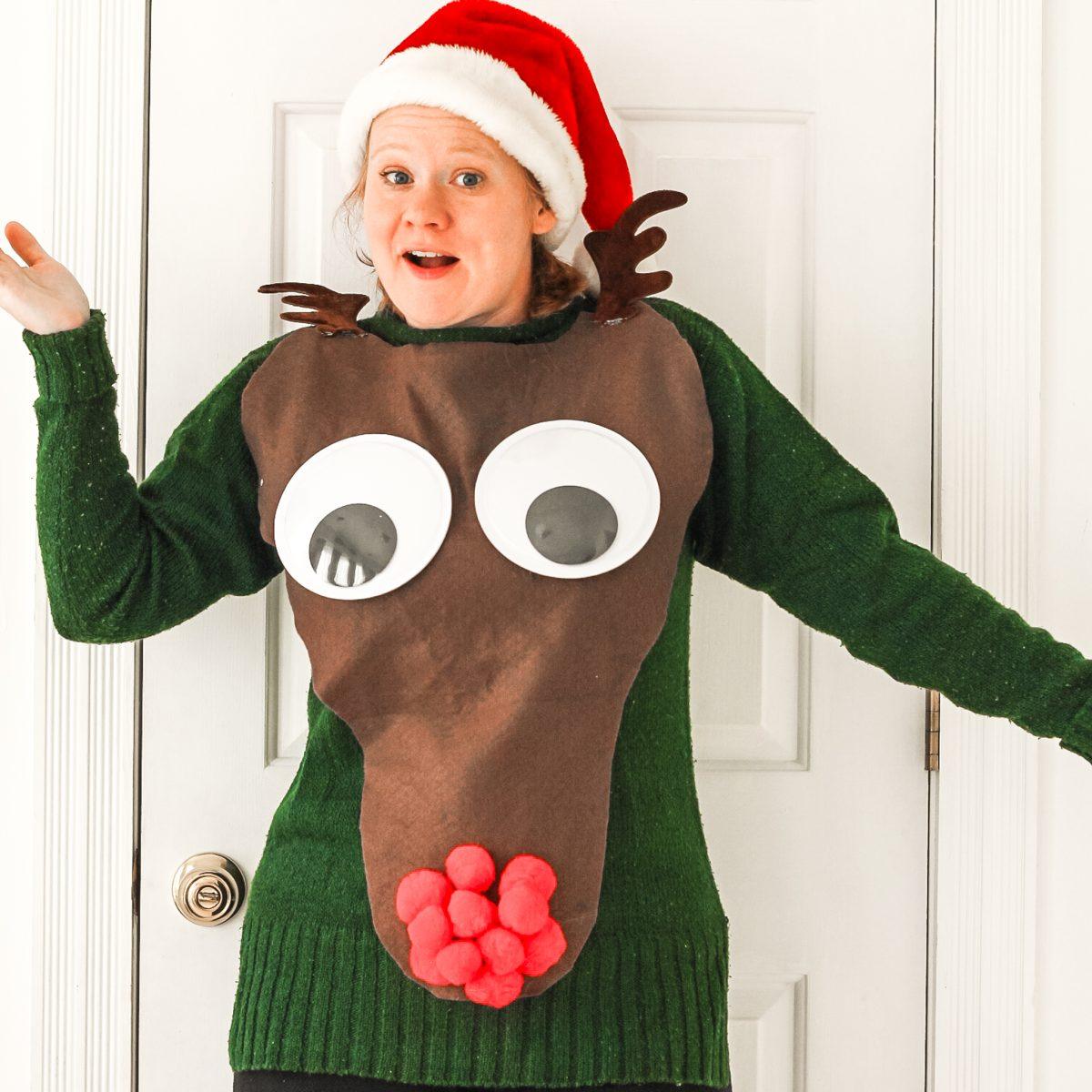 A woman in a Santa hat wearing a green sweater with a big brown felt reindeer head, giant googly eyes and a red pom pom nose