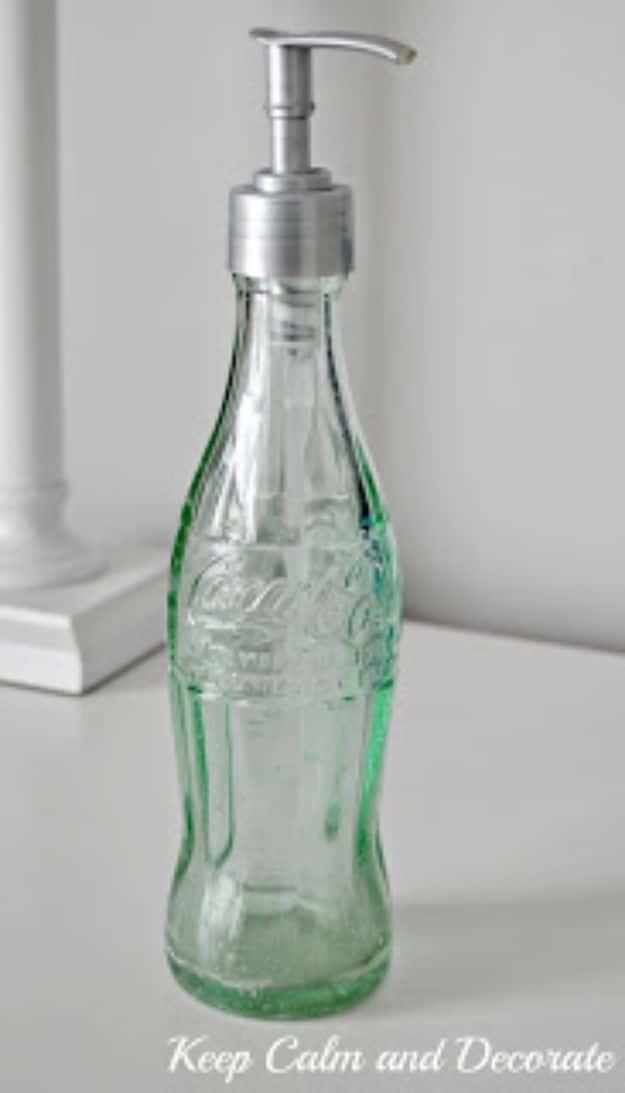 Vintage green glass Coke bottle used as a soap dispenser with a tall silver pump on a white painted surface