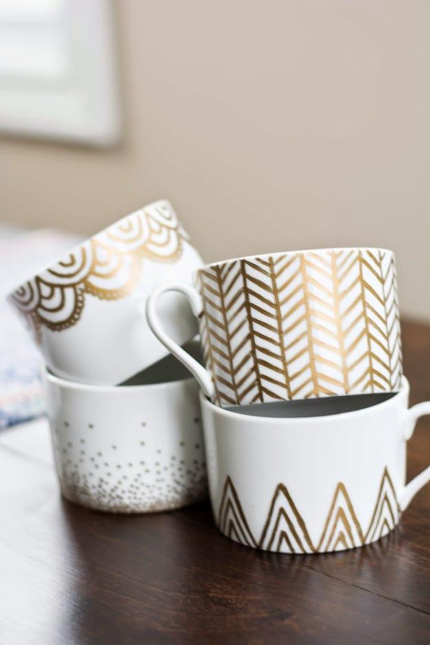 Gold sharpie mugs, four white mugs marked in gold with scallops herringbone dots and triangles on a dark table