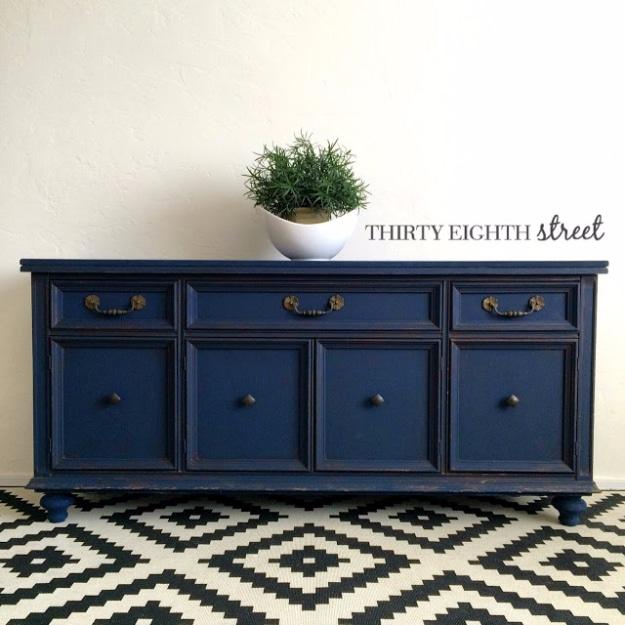 Navy blue painted console made from a china hutch base, with antique brass pulls on a black and white geometric rug