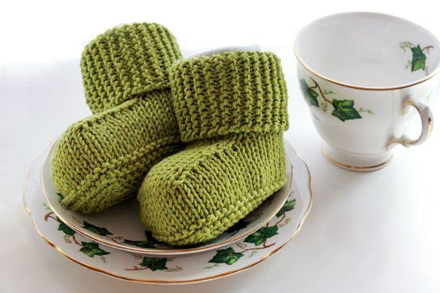Two pairs of olive green knitted baby Ugg style booties with folded cuffs, stacked on a floral china saucer