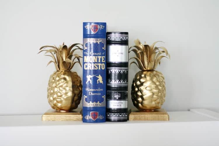 Pair of gold spray painted pineapple bookends on wood blocks holding two hardcover classic books upright