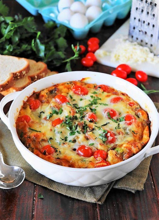 Savory breakfast bread pudding baked golden in a white dish with tomatoes, greens and melted cheese on top