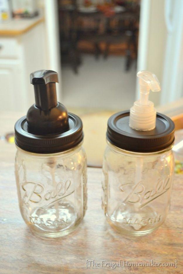 Two clear Ball mason jar soap dispensers with dark lids, one with a bronze pump and one with a clear plastic pump
