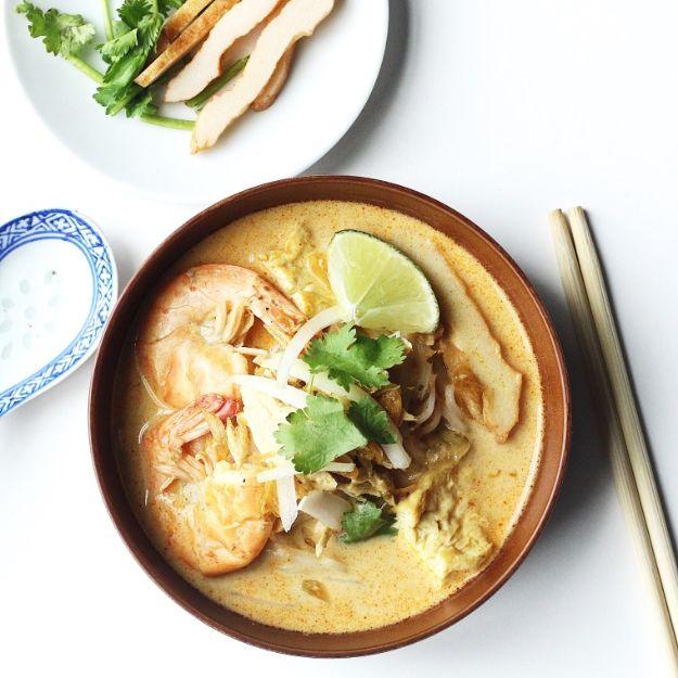 Chicken laksa in a brown bowl with shrimp, shredded chicken, rice noodles, lime wedge and chopsticks