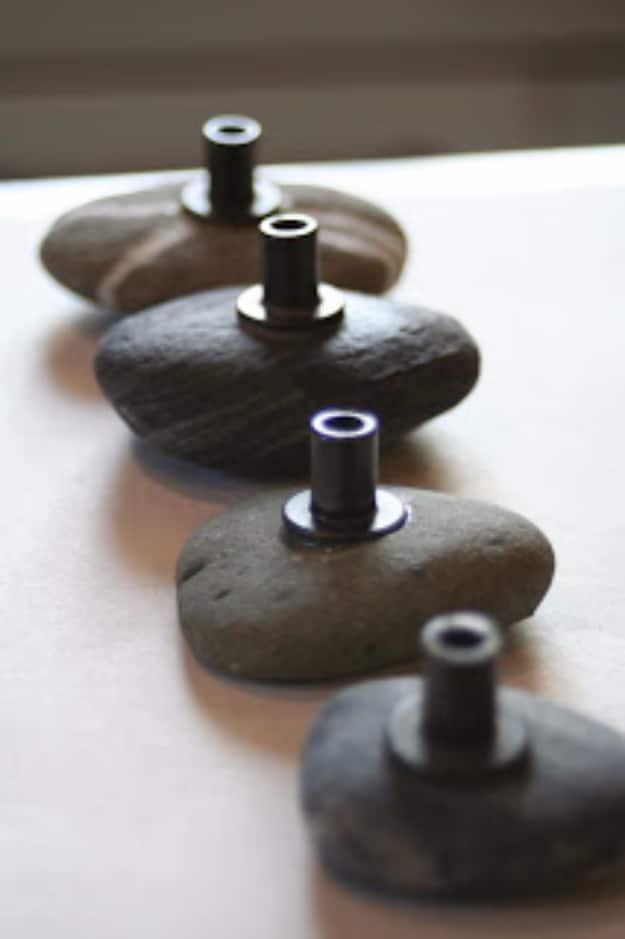 Four flat river stones fitted with dark machine bolt hardware to make cabinet knobs, lined up on a white surface