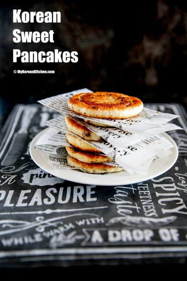 Korean sweet pancakes, hotteok, stacked on a plate on newspaper print with golden fried crisp brown edges