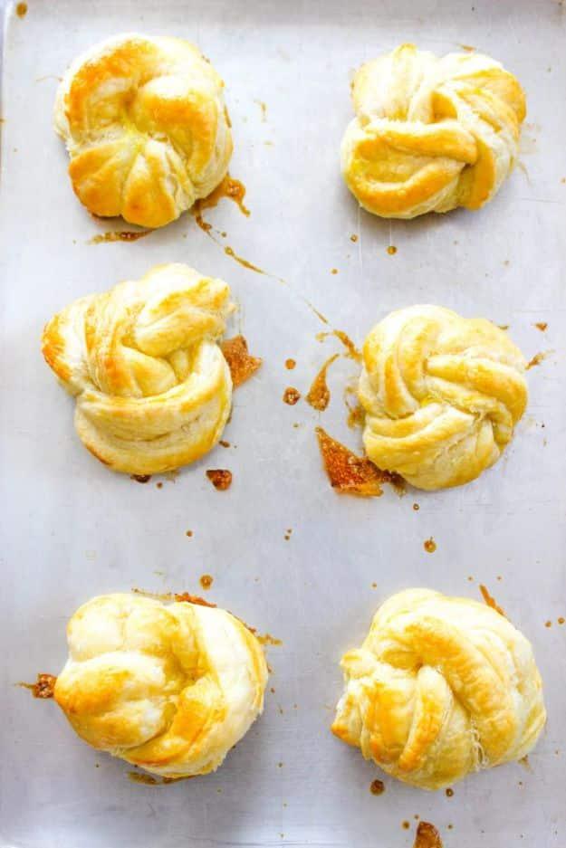 Six golden puff pastry coconut knots cooling on a parchment lined baking sheet straight from the oven