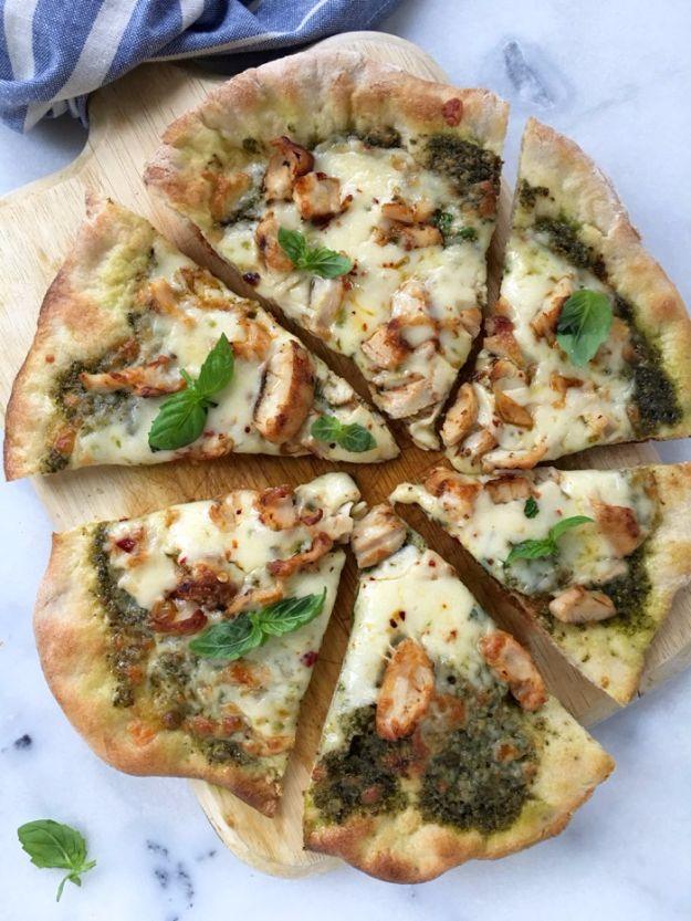 Chicken pesto pizza cut into slices with green walnut pesto, pepper jack cheese and fresh basil on marble