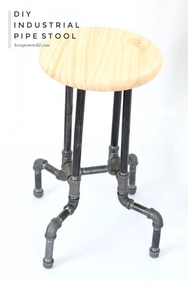 DIY industrial pipe stool with a pale round wood seat on a flared black pipe base photographed on a white background