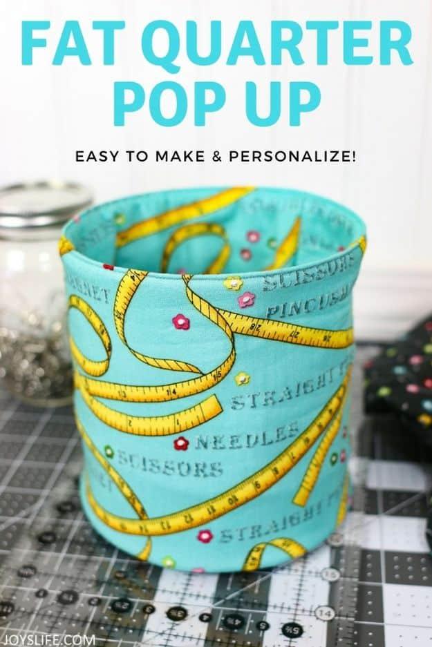 Fat quarter pop up fabric bucket in a teal tape measure and scissors print, set on a cutting mat under a typeset title