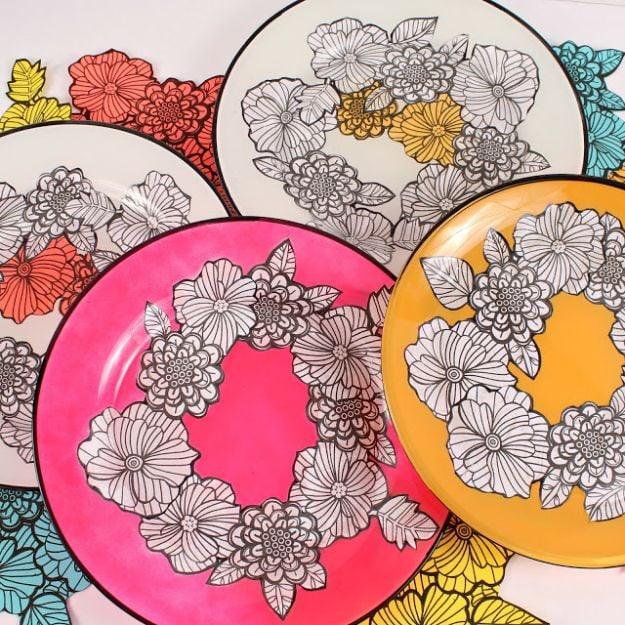 Four glass plates in pink, orange and turquoise with black outlined floral coloring book designs decoupaged on