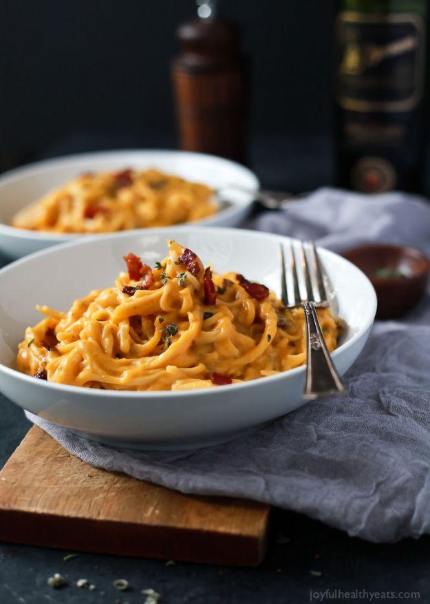 Creamy butternut squash alfredo pasta in two white bowls with bacon pieces and herbs over golden spaghetti