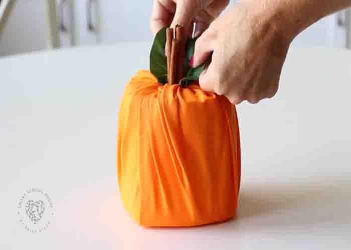 Finishing off the toilet paper pumpkin by inserting a silk leaf on top