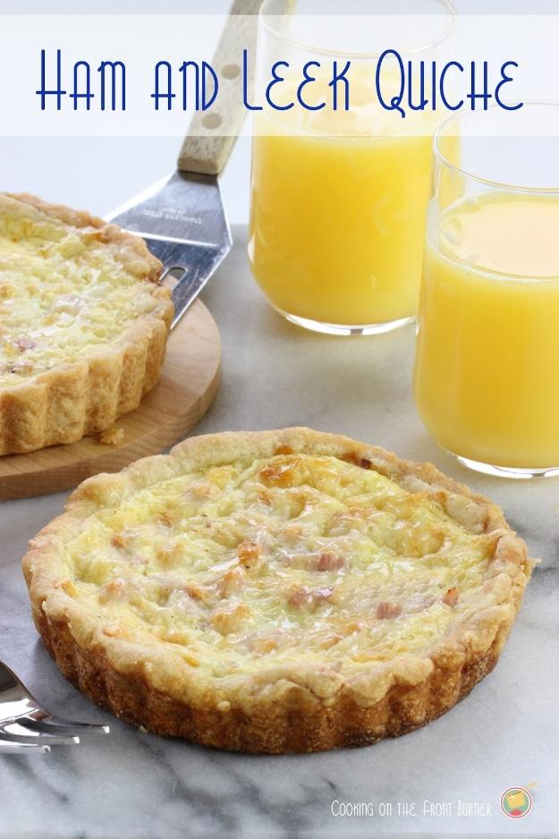 Typeset pin graphic of a small ham and leek quiche with a golden fluted crust on marble with two glasses of juice