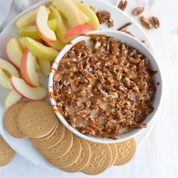 Salted caramel pecan cheesecake dip in a bowl with caramel drizzle and pecans beside graham crackers
