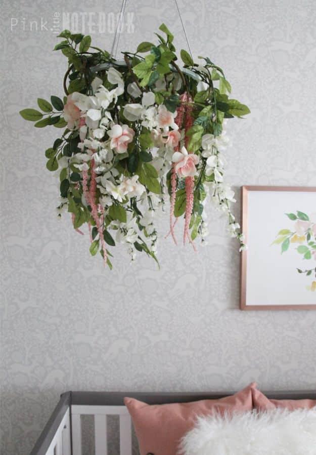 Floral chandelier of white blooms and trailing greenery hanging from a ceiling above a crib and framed art