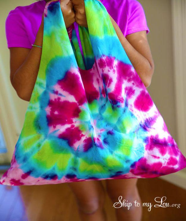 Child holding up a bright tie dyed t-shirt bag in pink, blue and green with the handles pinched together, face not in frame