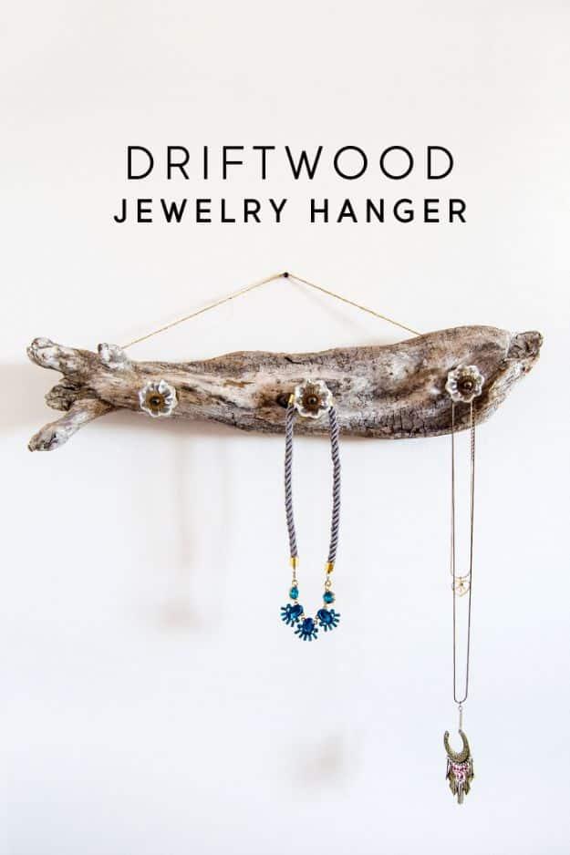 Pale driftwood branch fitted with crystal knobs holding three beaded necklaces, hung on a white wall