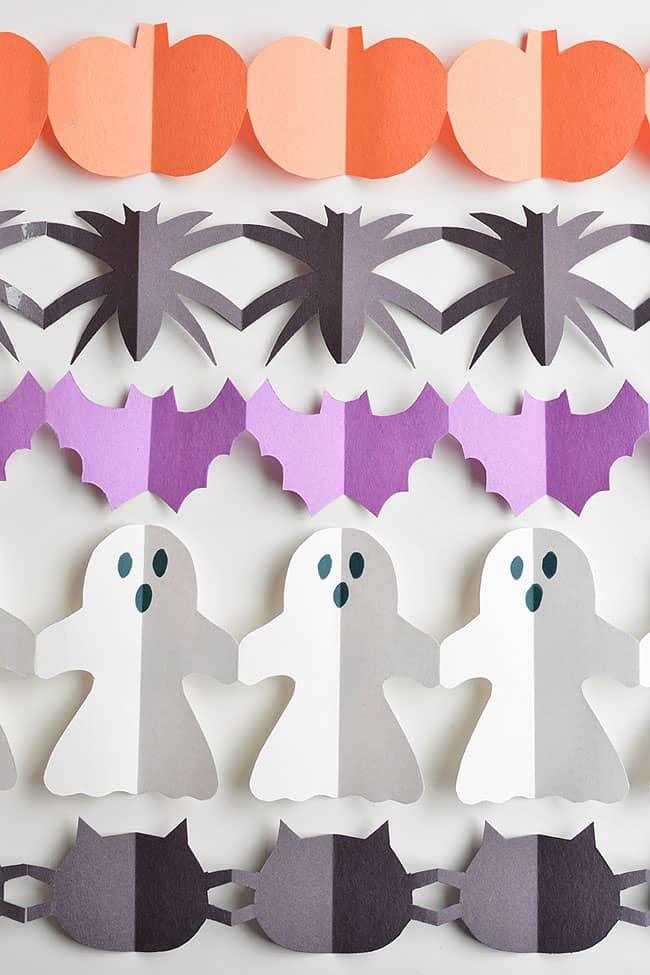 Orange pumpkins, black spiders, purple bats, white ghosts and black cats arranged as connected paper Halloween garlands