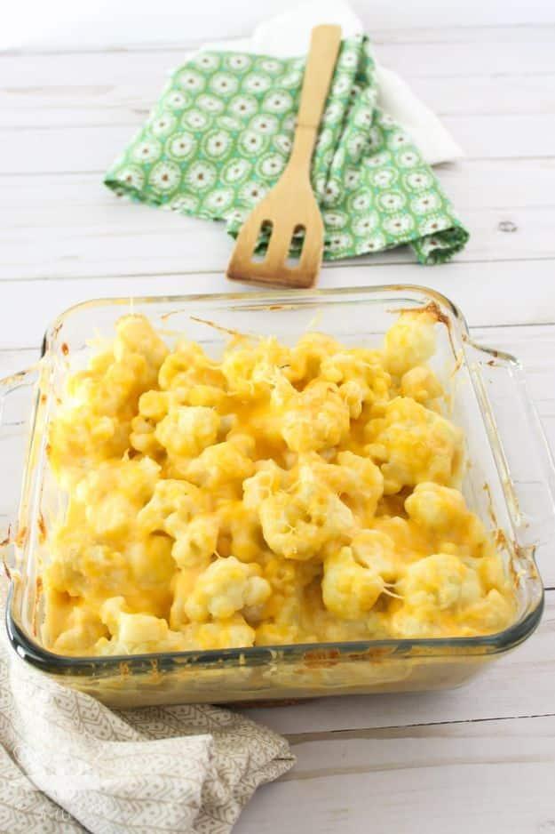 Cheesy cauliflower casserole with a pale cheese sauce in a square glass dish beside a green cloth napkin