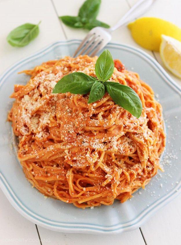 Creamy tomato angel hair pasta twirled on a plate with fresh basil leaves and lemon wedges alongside