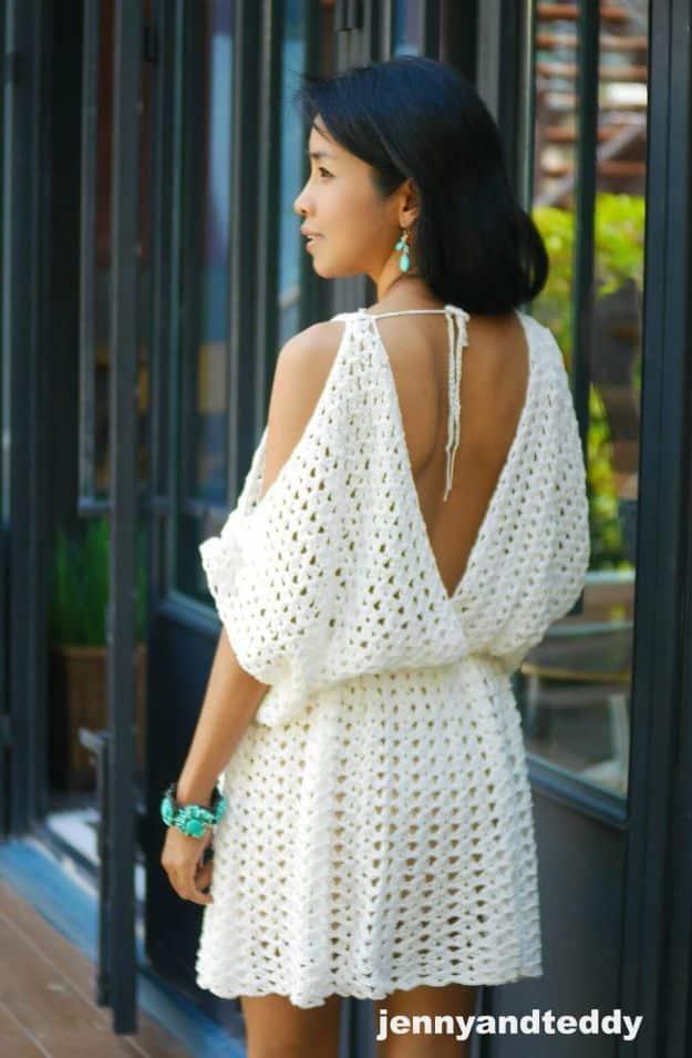 Woman outdoors in a white open crochet lace mini dress with a cold shoulder neckline and open tie back