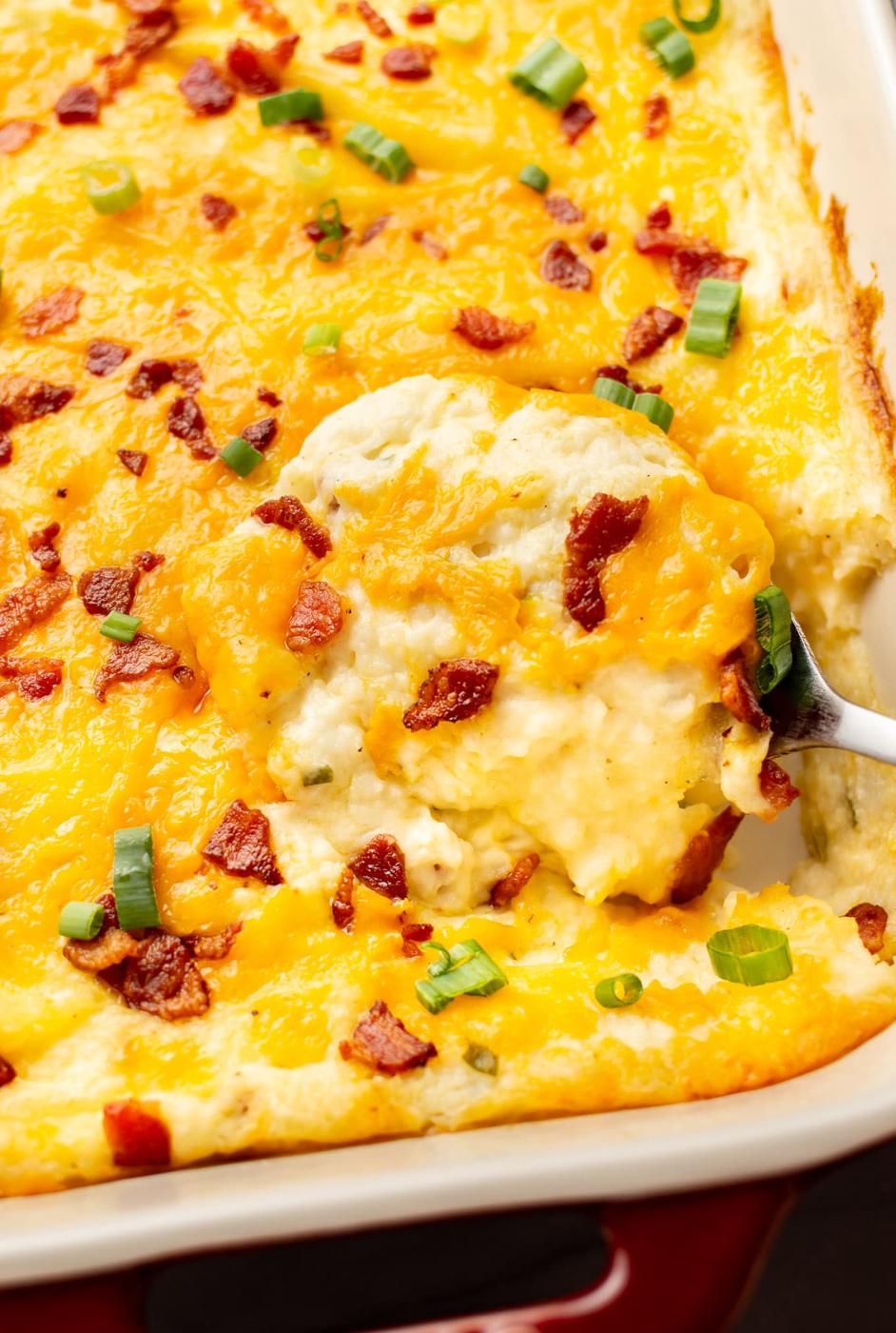 Loaded mashed potato casserole with melted cheddar, crumbled bacon and sliced green onion in a baking dish