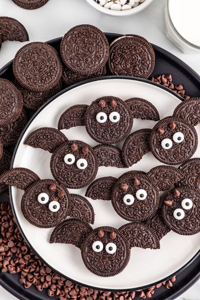 Oreo bat cookies with sandwich-cookie wings, candy eyes and small pointed ears arranged on a Halloween plate