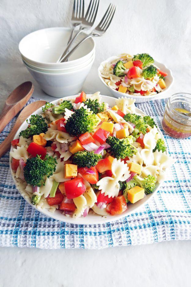 Broccoli cheddar pasta salad with bow tie pasta, red pepper and cubed cheddar in a bowl on blue checked cloth