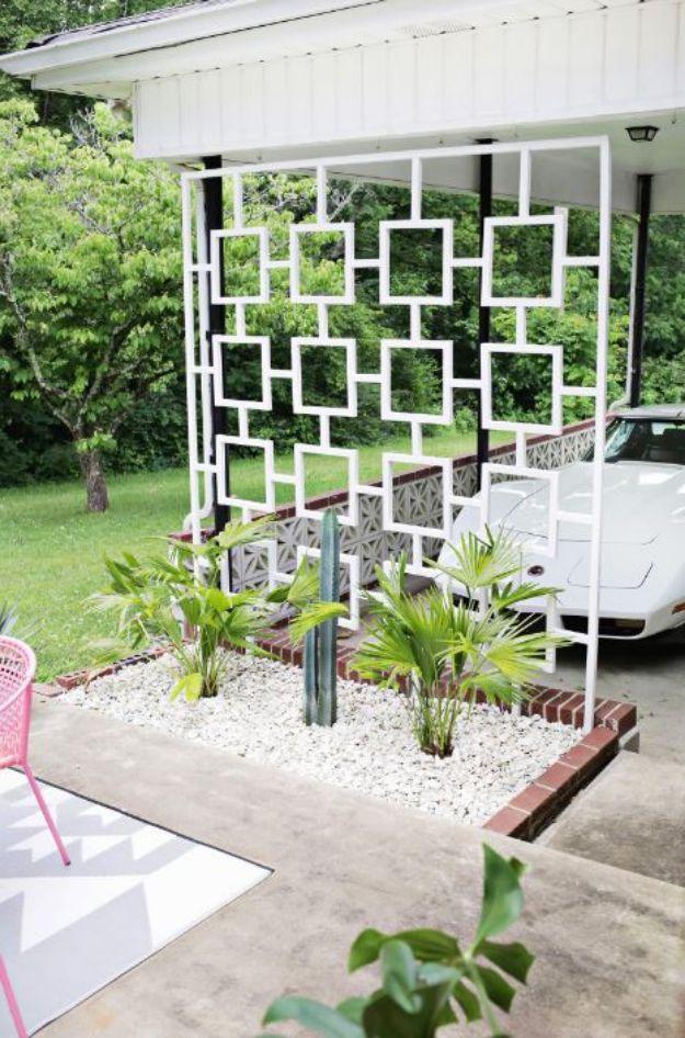 White geometric trellis screen of open squares hung beside a carport, over a white gravel bed planted with fan palms